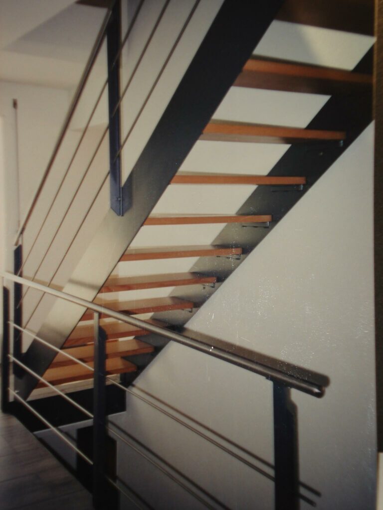 Treppe mit einbrennlackierten Wangen und Pfosten, Chromstahlseilen und Chromstahlhandlauf / Tritte aus Holz